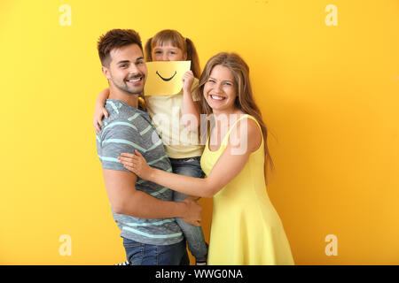 Portrait of happy family with drawn smile on sheet of paper against color background Stock Photo