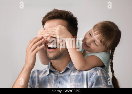 Happy little daughter covering eyes of her father at home Stock Photo