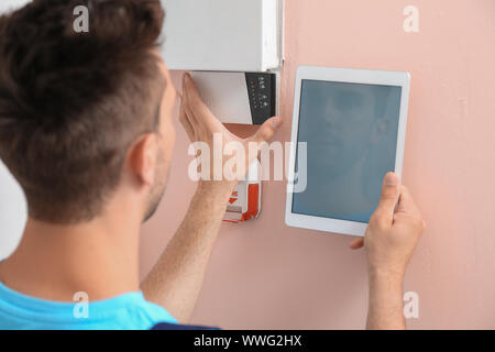 Electrician with tablet computer checking alarm system indoors Stock Photo