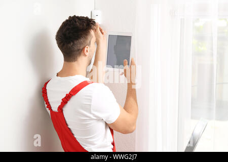 Electrician with tablet computer installing alarm system indoors Stock Photo