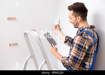 Electrician with tablet computer installing alarm system indoors Stock Photo