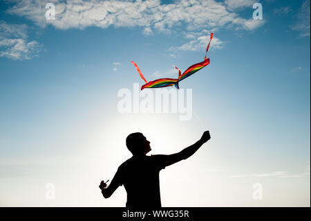 freedom concept of adult active man holding flying multicolored kite in blue sky in summer Stock Photo