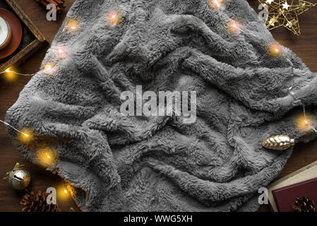 Cozy home and winter hygge concept. Seasonal winter and Christmas composition with grey soft plaid, garland, coffee, fresh cinnamon bun, pine cones on Stock Photo