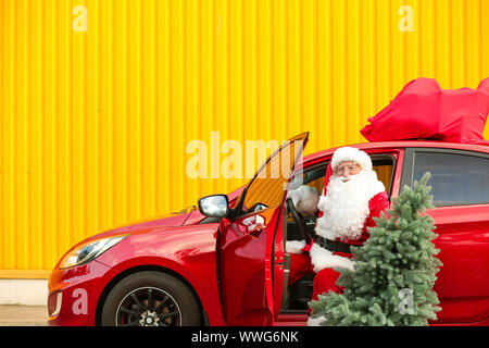 Santa Claus with fir tree getting out of car outdoors Stock Photo