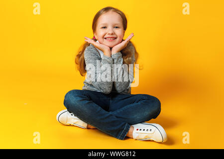 Portrait of a beautiful cute attractive charming cheerful little girl. A child sits on the floor and smiles. Stock Photo