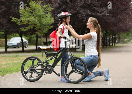 Mother helping her daughter to put on bicycle helmet outdoors Stock Photo