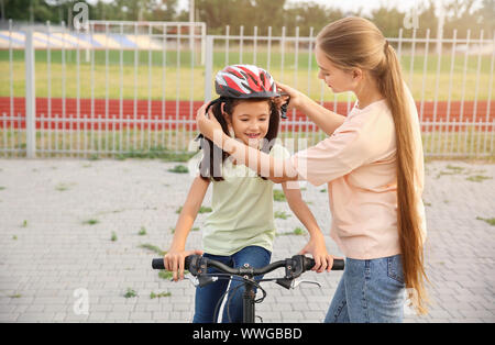 Mother helping her daughter to put on bicycle helmet outdoors Stock Photo