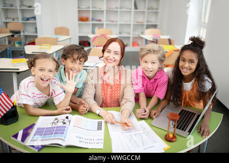 Children standing around their friendly smiling teacher Stock Photo