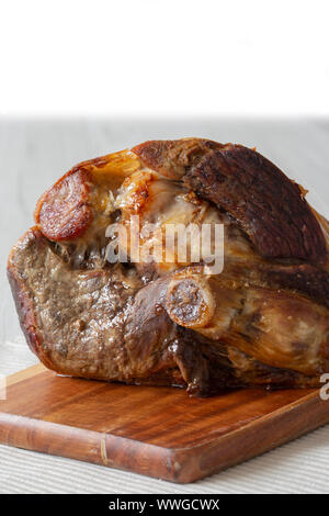 Roasted leg of lamb resting on a wooden chopping board and place mat.  Grey wood background Stock Photo