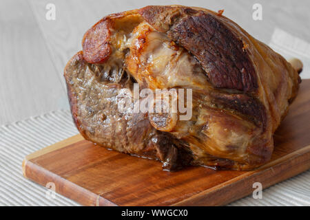 Roasted leg of lamb resting on a wooden chopping board and place mat.  Grey wood background Stock Photo