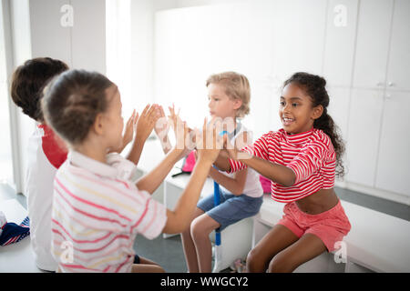 Boys and girls clapping their hands while sitting in locker room Stock Photo