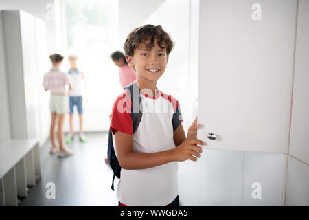 Dark-haired schoolboy standing near locker at school Stock Photo