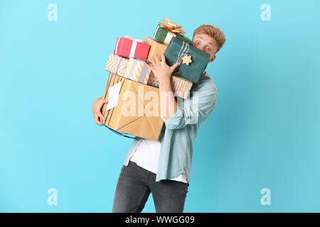 Young man with many gift boxes on color background Stock Photo