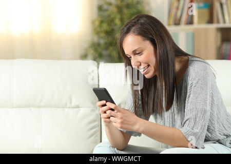 Happy woman using a smart phone sitting on a couch in the living room at home Stock Photo