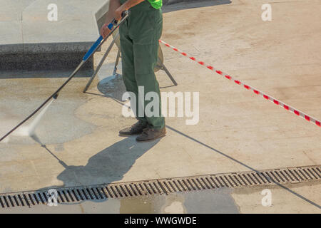 Worker man in uniform washes street or square. Municipal service of city cleaning process. Guy uses water spray equipment Stock Photo
