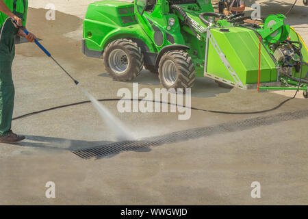 Worker man in uniform washes street or square. Municipal service of city cleaning process. Guy uses water spray equipment and machine Stock Photo