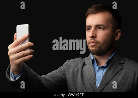 Young modern man in suit using facial recognition on smartphone Stock Photo