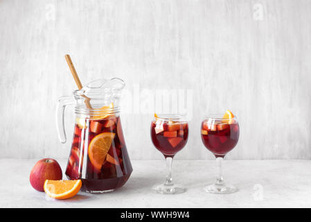 Red wine sangria or punch with fruits and ice in glasses and pitcher. Homemade refreshing fruit sangria on white background, copy space. Stock Photo