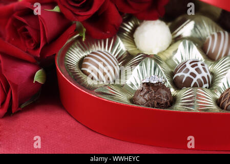 Diamond engagement inside of a heart shaped box of chocolate truffles with red roses. Selective focus on diamond ring with soft blurred background. Stock Photo