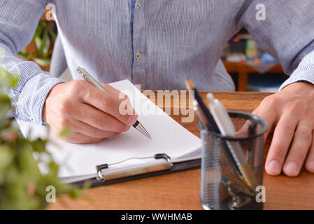Man starting to write on blank sheet in a folder sitting in front of a table. Horizontal composition. Front elevated view. Stock Photo