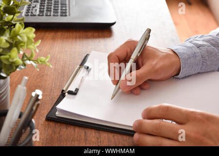 Man writing on a blank sheet of paper in a folder on a wooden table in the office. Horizontal compositon. Elevated view. Stock Photo