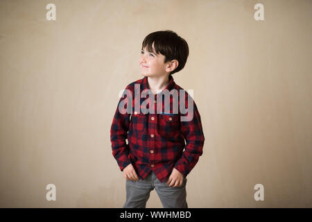 cute fashionable small boy smiling wearing blue red plaid shirt and grey pants with hands in pockets Stock Photo