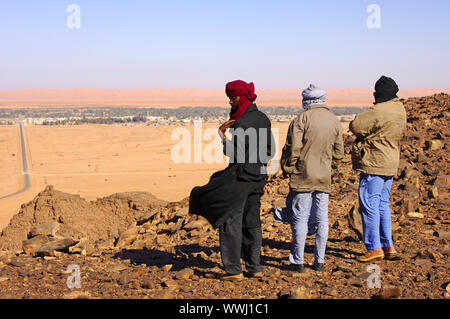 Native men in Arabic dress with traditional headscarf looking from a hill to the desert town of Germa in the plain Stock Photo