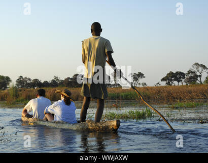 Boat driver with tourists in the traditional Mokoro dugout on excursion in the Okavango Delta Stock Photo