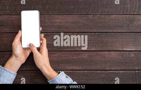 Smartphone with blank screen in woman's hands on wooden background Stock Photo