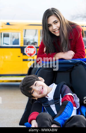 Big sister with disabled brother in wheelchair by school bus Stock Photo