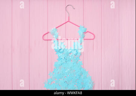 Blue girls stylized dress from stars confetti hanging on red trempel on pink wooden background. Fashion concept Stock Photo