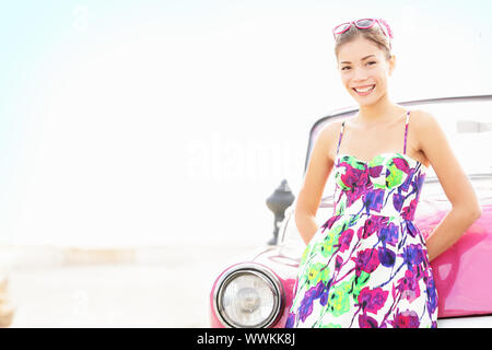 Car woman smiling happy standing in front of pink retro vintage car. Portrait of pretty girl in summer dress.  Multicultural Chinese Asian / Caucasian Stock Photo