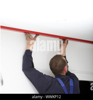 Man using a large red spirit level on the ceiling in a DIY home maintenance concept Stock Photo