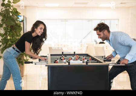 two young colleagues brunette beautiful woman and handsome man playing table football during break at the office looking excited Stock Photo
