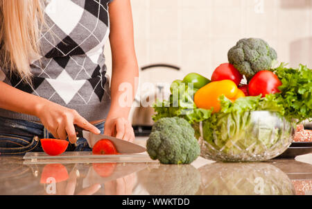 Woman cutting up tomato in kitchen for meal. Horizontal shot. Stock Photo