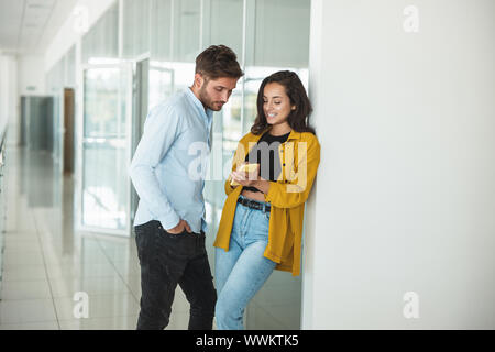 two young colleagues handsome man and beautiful woman flirting together at the office she shows him something in smartphone Stock Photo