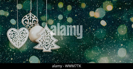 Hanging white Christmas baubles in a nordic style with blurred lights, sparks and snow on a dark greenish blue background. Copy space Stock Photo