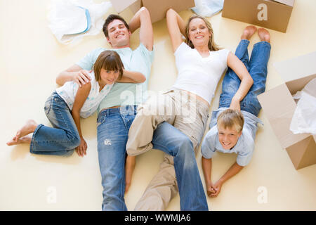 Family lying on floor by open boxes in new home smiling Stock Photo