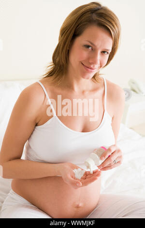 Pregnant woman in bedroom with medicine smiling Stock Photo