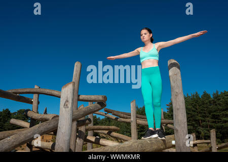 Sporty woman balancing on a wooden beam on an outdoor assault course Stock Photo