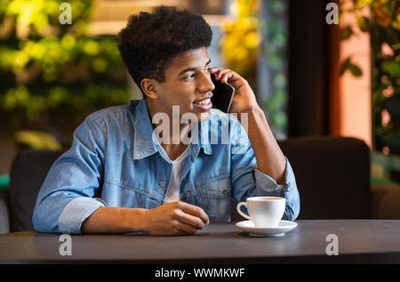 Young afro guy talking on smartphone, looking aside Stock Photo