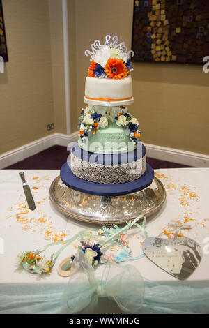 Wedding Cake, three tiered wedding cake decorated with flowers and decorative icing, on a cake stand with a knife waiting to be cut. Stock Photo