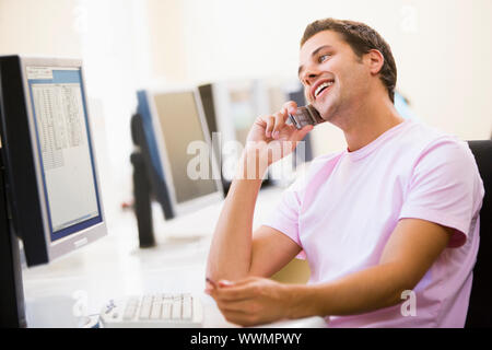 Man sitting in computer room using cellular phone and smiling Stock Photo