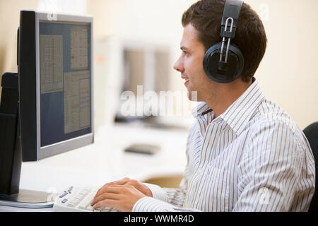 Man wearing headphones in computer room typing and smiling Stock Photo