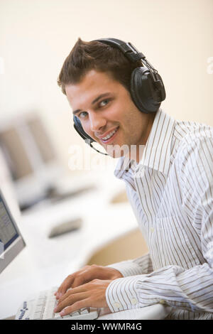 Man wearing headphones in computer room typing and smiling Stock Photo