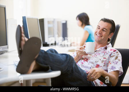 Man in computer room with feet up drinking coffee and smiling Stock Photo