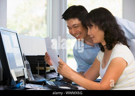 Couple in home office with computer and paperwork smiling Stock Photo