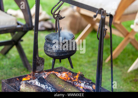 Rusty old cooking pot simmering over open fire at a campsite. Stock Photo