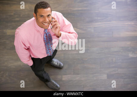 Businessman standing indoors using cellular phone smiling Stock Photo