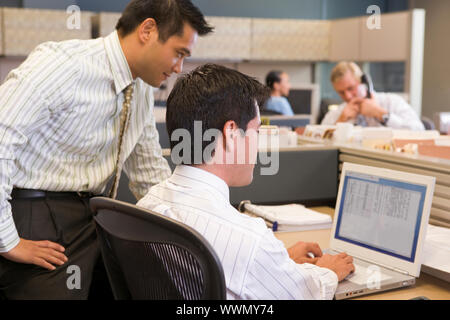 Two businessmen in cubicle looking at laptop Stock Photo